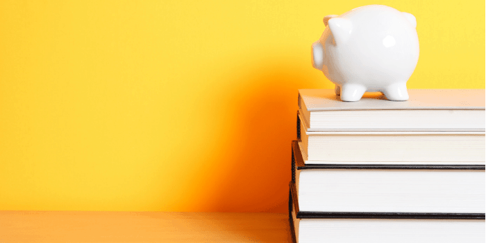 A piggy bank on top of a stack of books with yellow background