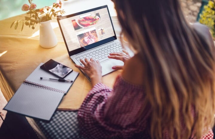 Young food blogger entrepreneur writing blog post and working online on laptop from home office