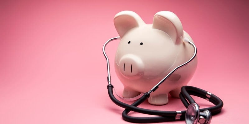This is a photo of a large white piggy bank on a pink background. This is a concept photo related to finance and the medical hospital industry,
