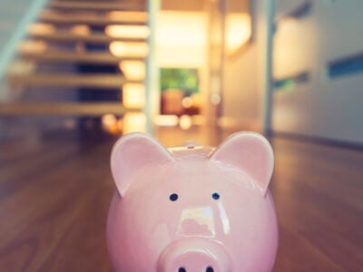 Saving for a home concept. Piggy bank standing at front door with house interior in the background. Pig is pink in foreground and house is modern style. Copy space.