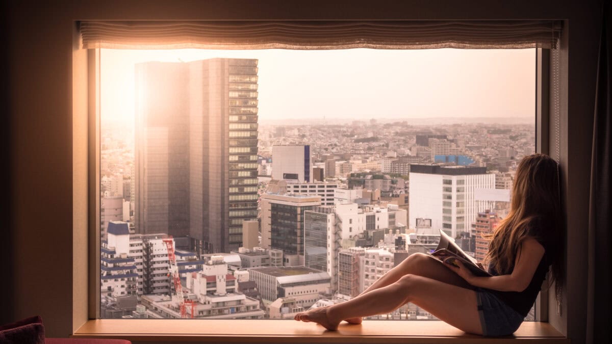 A woman is relaxed and looking out of her hotel window. She's looking at the cityscape of Shibuya, Tokyo, Japan below. Shot in the morning in Spring.